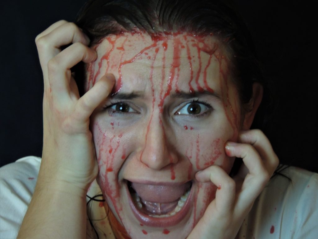 A woman clutching her face and screaming, with blood covering her face.