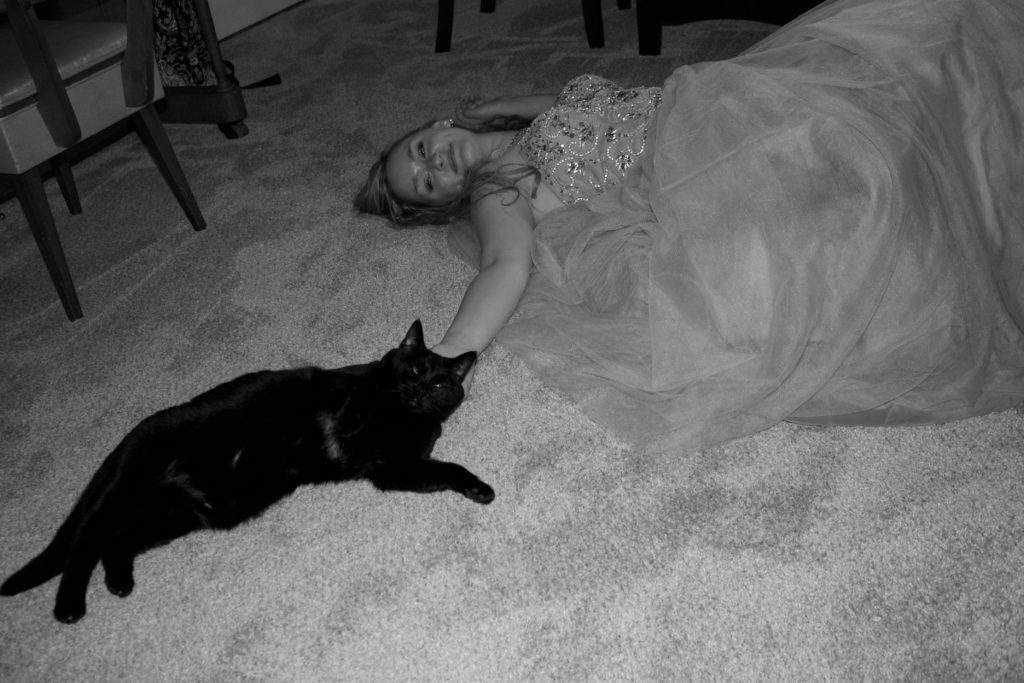 the author's cat Lucy and her laying on her living room floor after senior prom, her cinderella ballgown spread out around her, circa 2016.